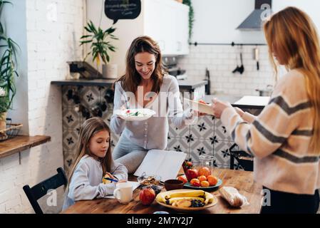 Zwei junge Frauen bereiten sich auf das Abendessen vor und decken den Tisch, während das Mädchen ihre Lektionen lernt. Stockfoto