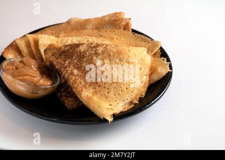 Frittierte Pfannkuchen in Dreiecksform mit Kondensmilch auf weißem Hintergrund Stockfoto