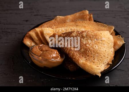 Foto mehrerer dreieckiger Pfannkuchen mit Kondensmilch auf einem runden Teller Stockfoto