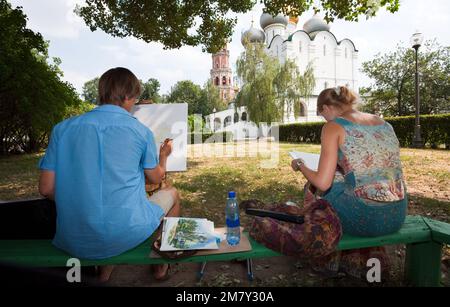 Moskau, Russland - 21. Juli 2010. Zwei junge Kunststudenten, die auf einer Bank sitzen und die Smolensk Kathedrale auf Leinwand zeichnen Stockfoto