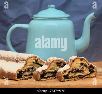 Stillleben mit geschnittenem Mohnstollen auf einem Holzbrett vor dunkelblauem Hintergrund Stockfoto