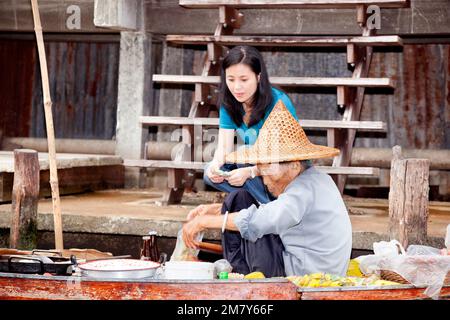 Damnoen Saduak, Thailand-9. August 2009: Eine ältere Frau verkauft Essen von seinem Boot auf einem schwimmenden Markt in der Nähe von Bangkok Stockfoto