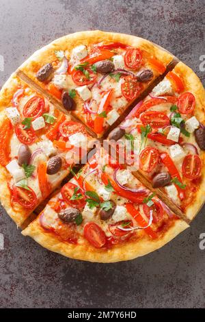 Leckere griechische Pizza auf einer dünnen Teigbasis, die auf dem Holzbrett auf dem Tisch geschnitten wurde. Vertikale Draufsicht von oben Stockfoto