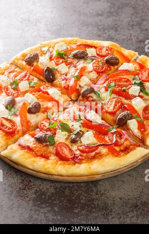 Leckere griechische Pizza auf einer dünnen Teigbasis, die auf dem Holzbrett auf dem Tisch geschnitten wurde. Vertikal Stockfoto