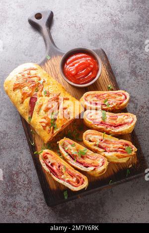 Hausgemachte Stromboli-Pizza mit Käse, Peperoni, Salami auf dem Holzbrett auf dem Tisch. Vertikale Draufsicht von oben Stockfoto