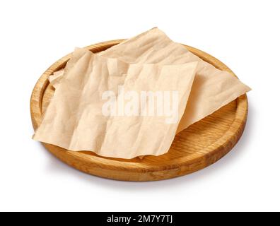 Backpapier auf Holzplatte isoliert. Rundes Brett mit zerknitterten Stücken braunem Pergament oder Backpapier auf weißem Hintergrund. Konstruktionselement. Stockfoto
