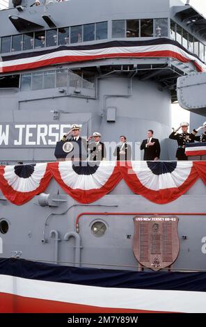 Die Gäste stehen auf der Rednerplattform, während die Nationalhymne während der Wiederinbetriebnahme des Schlachtschiff USS NEW JERSEY (BB-62) gespielt wird. Von links nach rechts sind der befehlshabende Offizier CAPT William M. Fogarty, ADM James D. Watkins, Leiter der Marineeinsätze, der Marineminister John F. Lehman Jr. und Präsident Ronald Reagan. Basis: Long Beach Naval Shipyard Bundesstaat: Kalifornien (CA) Land: Vereinigte Staaten von Amerika (USA) Stockfoto