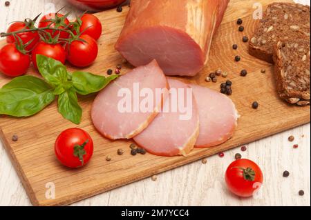 Schinken auf einem Holzbrett mit Tomaten und Basilikum Stockfoto