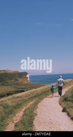 Ein vertikales Bild von einem Mann und einem Kind, die einen Fußweg entlang zur Beachy Head Klippe und ihrem Leuchtturm in Sussex, England, gehen Stockfoto