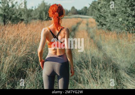 Junge Frau im Trainingsanzug läuft die Straße entlang, Blick von hinten Stockfoto