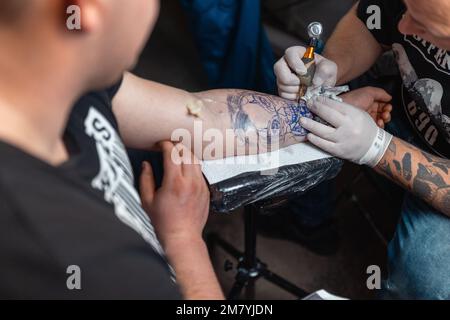 Ein junger Mann bekommt ein frisches Tattoo auf seinem Arm bei einer Tattoo-Konferenz Stockfoto