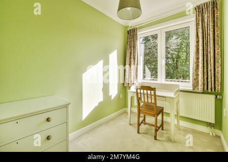 Ein Raum mit grünen Wänden und weißen Verzierungen an den Fensterbänken, es gibt einen kleinen Schreibtisch vor dem Fenster Stockfoto