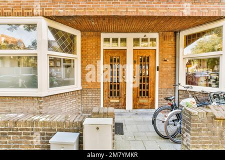 Ein Backsteinhaus mit einem Fahrrad, das an der Vordertür geparkt ist und zwei Fenster an der Seite des Hauses, Stockfoto