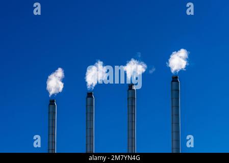 Vier Stahlschornsteine mit weißem Rauch über klarem blauen Himmel; Energie- und Umweltschutzkonzept; Kopierraum Stockfoto