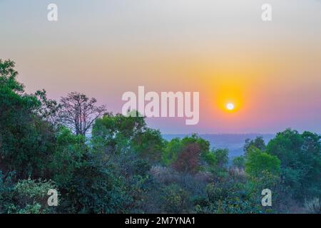 Ein Sonnenuntergang über einem Berg. Die Sonnenstrahlen auf den Gipfeln erzeugen eine Reihe von Farben, von warmen Orangen und Gelbtönen bis hin zu kühlen Purpur und Blau. Stockfoto