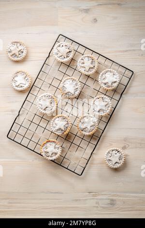 Flach liegende Hackkuchen mit Gebäcksternen, mit Puderzucker bestäubt auf weißem Holzgrund: Weihnachtsbäckerei. Stockfoto