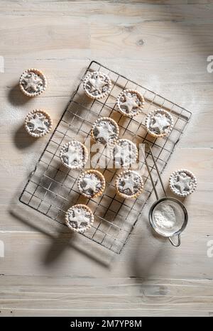 Flacher Hackkuchen mit Backsternchen, mit Puderzucker auf weißem Holzhintergrund bedeckt: Weihnachtliches Backwaren. Stockfoto