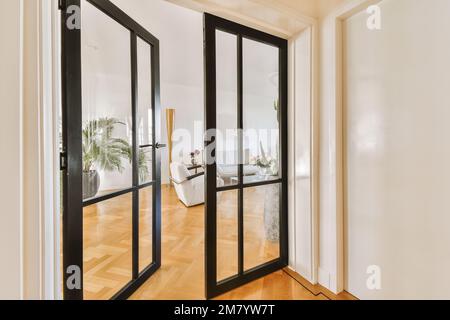 Das Innere eines Hauses mit Holzfußboden und schwarzen Doppeltüren führt zu einem offenen Wohnzimmer auf einer Seite Stockfoto