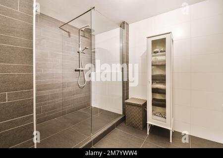 Ein modernes Badezimmer mit grauen Fliesen und weißen Fliesen an den Wänden, zusammen mit einer begehbaren Duschkabine Stockfoto