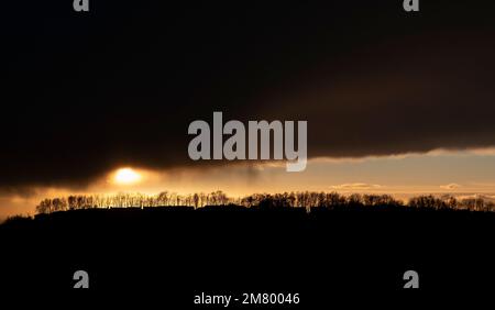 Dunkle Sturmwolken hängen über einem hellen Himmelsstreifen, während die Wintersonne untergeht, Worcestershire, England. Stockfoto