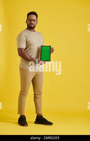 Porträt eines positiven Mannes in voller Länge, der einen Tablet-Computer mit grünem Bildschirm zeigt Stockfoto