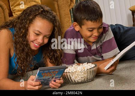 Ein junges Mädchen und ein Junge, die zu Hause auf dem Boden liegen und zusammen einen DVD-Film aussuchen Stockfoto