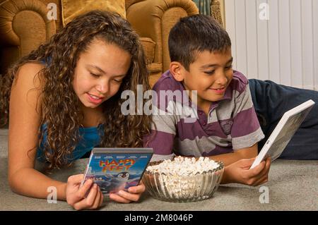 Ein junges Mädchen und ein Junge, die zu Hause auf dem Boden liegen und zusammen einen DVD-Film aussuchen Stockfoto