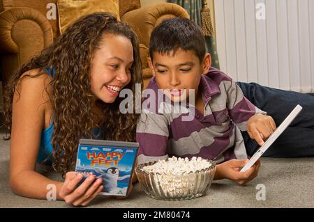 Ein junges Mädchen und ein Junge, die zu Hause auf dem Boden liegen und zusammen einen DVD-Film aussuchen Stockfoto