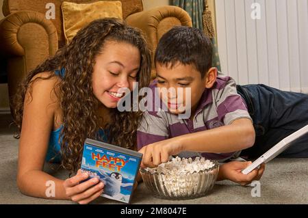 Ein junges Mädchen und ein Junge, die zu Hause auf dem Boden liegen und zusammen einen DVD-Film aussuchen Stockfoto