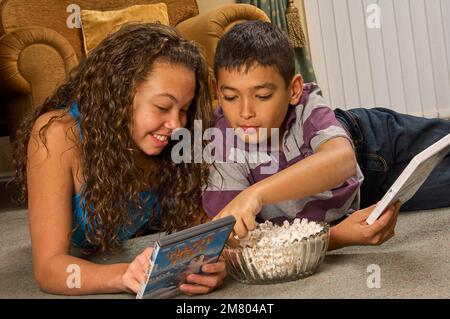 Ein junges Mädchen und ein Junge, die zu Hause auf dem Boden liegen und zusammen einen DVD-Film aussuchen Stockfoto