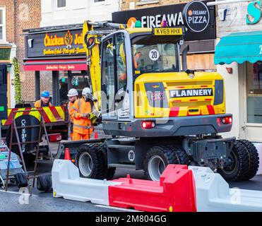 Digger betrieben von Flannery, parkt in der London Street und mehrere Arbeiter in Warnjacken und Schutzhelmen Stockfoto