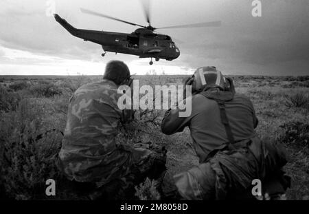 Zwei Spezialmannschaften der US Navy (USN) beobachten, wie ein USN Sikorsky SH-3 Sea King Helicopter während einer Kampfübung zur Suche und Rettung (SAR) auf dem Luftwaffenstützpunkt Mountain Home (AFB), Idaho (ID) startet. Basis: Mountain Home Luftwaffenstützpunkt Staat: Idaho (ID) Land: Vereinigte Staaten von Amerika (USA) Stockfoto