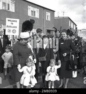 1960er, historisch, Dudelsackband spielt auf der Straße, während eine Dame von der Heilsarmee in Kanada einen Blick auf das Twon/Village, Fife, Schottland, Großbritannien, gibt. Stockfoto