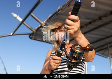 Die Frau fischt auf einer rotierenden Stange im Meer von der Yacht aus bei windigem Wetter. Stockfoto