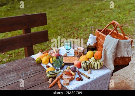 Picknick im Herbstpark. Essen, Getränke, Picknickkorb auf einem Holztisch im Garten. Gemütliche Mittagsatmosphäre. Kürbis, Kuchen und Wein auf dem Tisch. Hohe Qualität über dem Foto Stockfoto