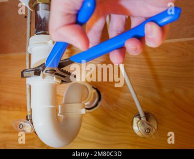 Nahaufnahme des Klempners mit einem verstellbaren Schraubenschlüssel zur Reparatur der Leckage im Abflussrohr des Waschbeckens. Stockfoto