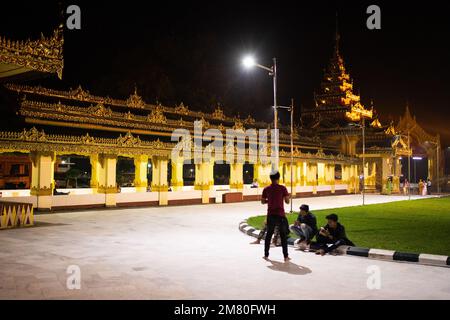 Tägliches Leben Myanmar - Menschen bei Nacht in der Nähe eines goldenen Tempels im Dorf Dawei. Dawei, Stockfoto