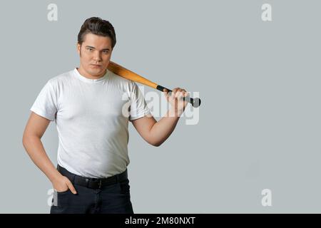 Ein stilvoller Mann hält einen Schläger auf seiner Schulter auf einem grauen, isolierten Hintergrund Stockfoto