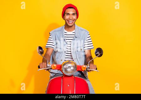 Foto in voller Länge von einem beeindruckenden süßen Kerl in Jeanskleidung, die lächelnd auf dem Fahrrad sitzt, isolierter gelber Hintergrund Stockfoto