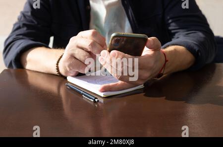 Ein Unbekannter hält ein Telefon in einer Hand und berührt den Bildschirm mit dem Finger Stockfoto