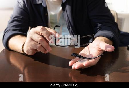 Die Hände eines Mannes halten einen zerbrochenen Brillenrahmen in den Handflächen Stockfoto