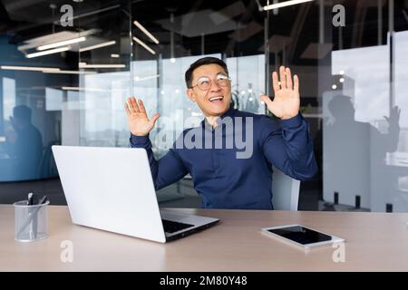 Glücklicher junger Geschäftsmann, der tanzt, während er am Laptop im Büro sitzt. Feiert Sieg, erfolgreichen Deal, finanziellen Erfolg. Stockfoto
