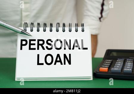 Geschäftskonzept. Auf einer grünen Oberfläche befindet sich ein Taschenrechner, ein Mann zeigt mit einem Stift auf ein Notizbuch mit der Aufschrift "persönlicher Kredit" Stockfoto