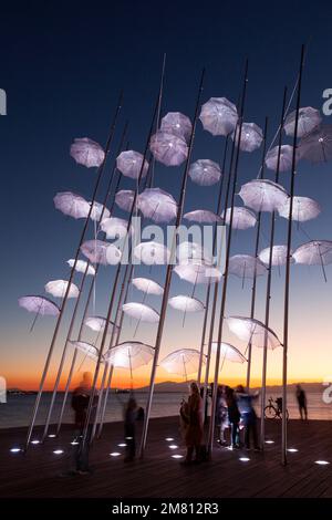 Menschen genießen die Sonnenuntergangsstunde in den berühmten Regenschirmen von Zongolopoulos, im Nea Paralia (Strandviertel) von Thessaloniki. Stockfoto
