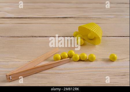 Gelbe Montessori-Kugeln mit Holzpinzette. Die Entwicklung der Feinmotorik im Kindesalter. Stockfoto