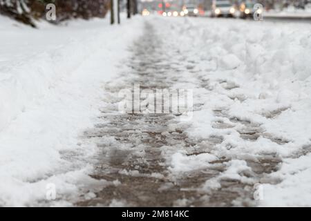 Winterstraße mit Salzschmelze. Nahaufnahme des Gehwegs mit Slush an verschneiten Tagen. Stockfoto