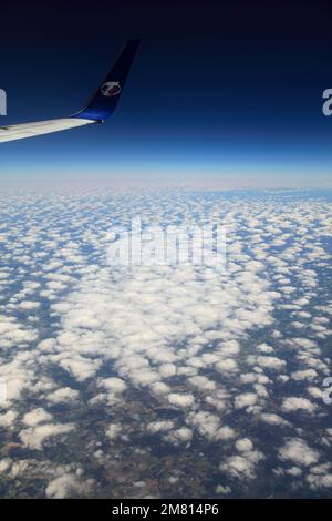 Blick vom Flugzeugfenster auf das TS Airlines Logo und den Flügel mit Altocumulus Stratiformis Wolken Stockfoto
