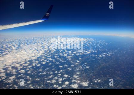 Blick vom Flugzeugfenster auf das TS Airlines Logo und den Flügel mit Altocumulus Stratiformis Wolken. Stockfoto