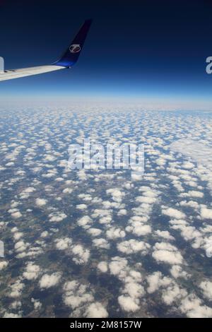 Blick vom Flugzeugfenster auf das TS Airlines Logo und den Flügel mit Altocumulus Stratiformis Wolken. Stockfoto