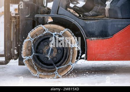 Traktorrad mit Kette. Traktor oder Lader auf einer rutschigen, verschneiten Straße. Lader fahren mit rutschfesten Ketten auf Schnee. Stockfoto